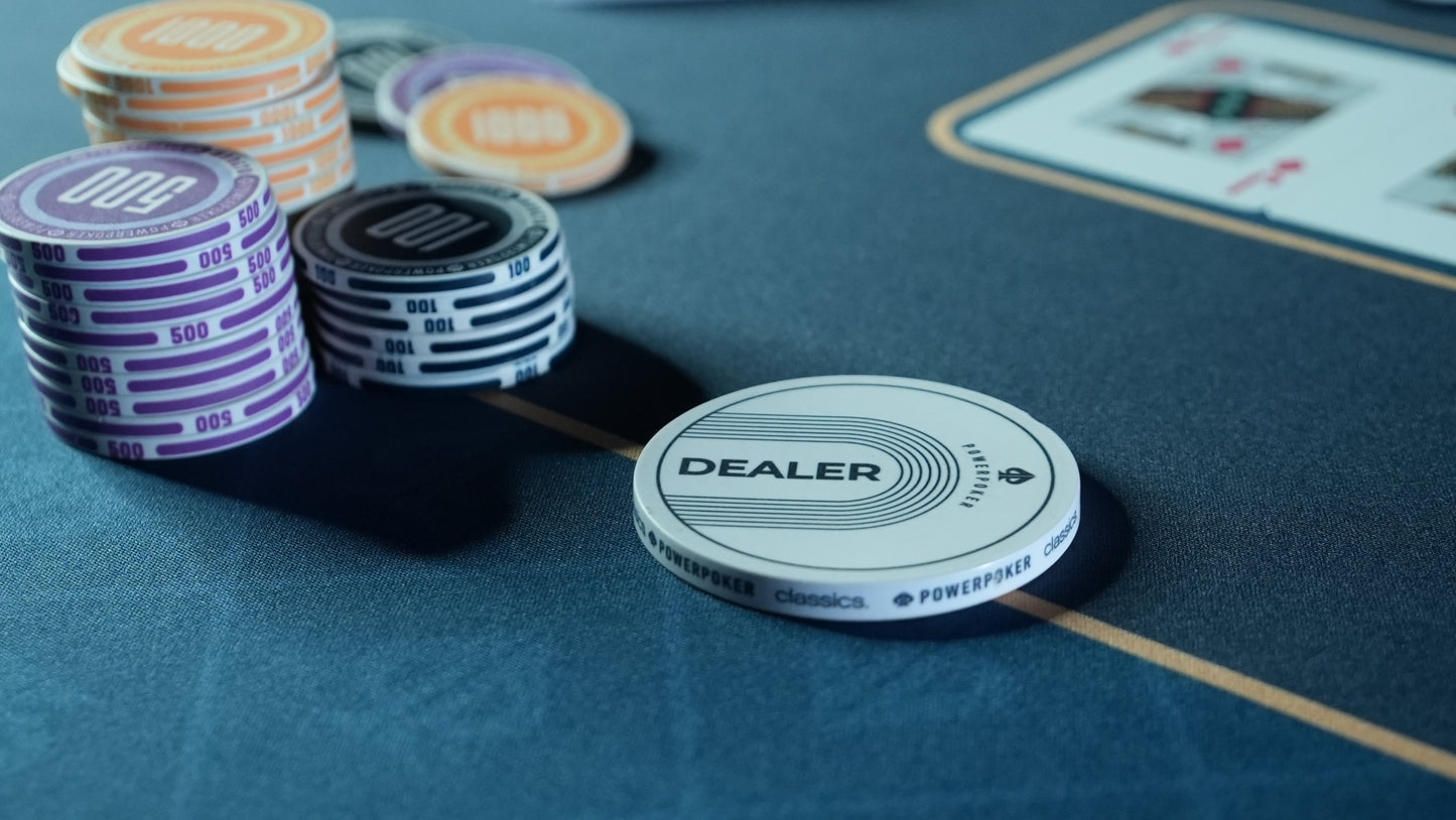 Nahaufnahme von gestapelten Pokerchips und einem weißen Dealrbutton auf der ausgerollten PowerPoker 'Pro Blue' XXL Pokermatte (200x100 cm) in petrol-blau aus rutschfestem Neopren während eines privaten Hobby-Spiels.
