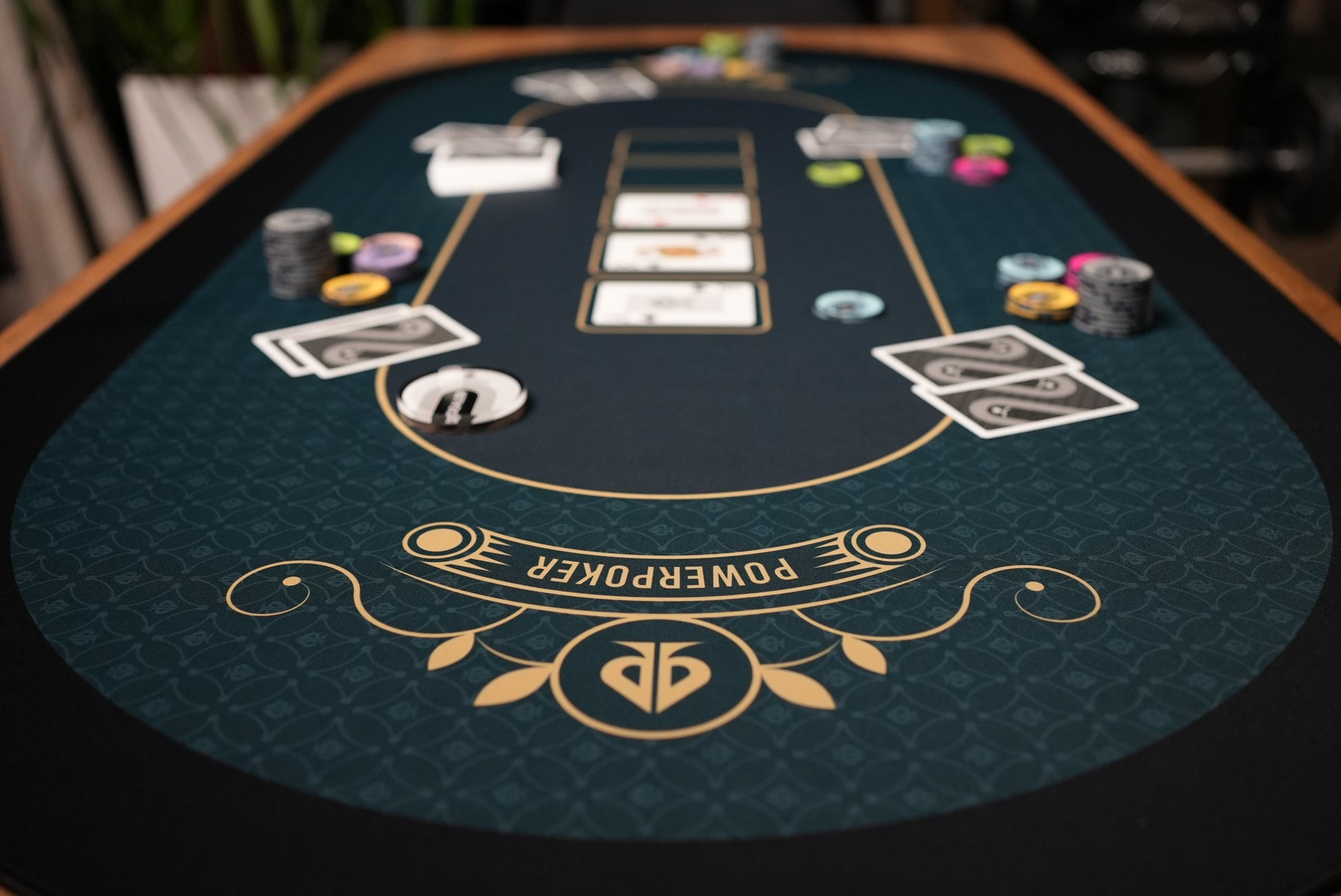 Beispielfoto zur Verwendung. Nahaufnahme Logo. Pokerchips, Karten und Dealerbutton im Hintergrund auf PowerPoker Pokermatte Royal Green.